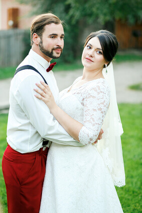 Couple élégant enlacé,  sur le côté aprèté avec la barbe, la moustache, la cravate ou le noeud papillon et des bretelles - la Jeune mariée dans la robe de mariage en blanc