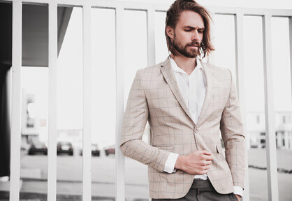 portrait of sexy handsome fashion male model man dressed in elegant beige checkered suit -posing on the street background
